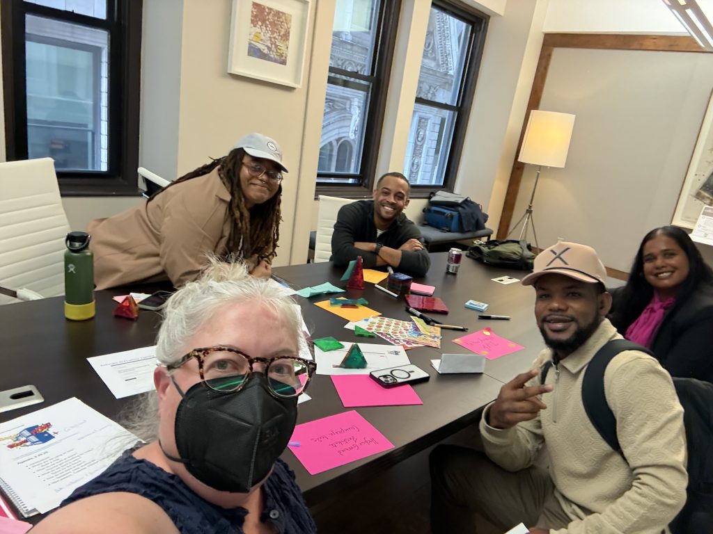 5 people working around a big table in an office, turned towards the camera for a group selfie.